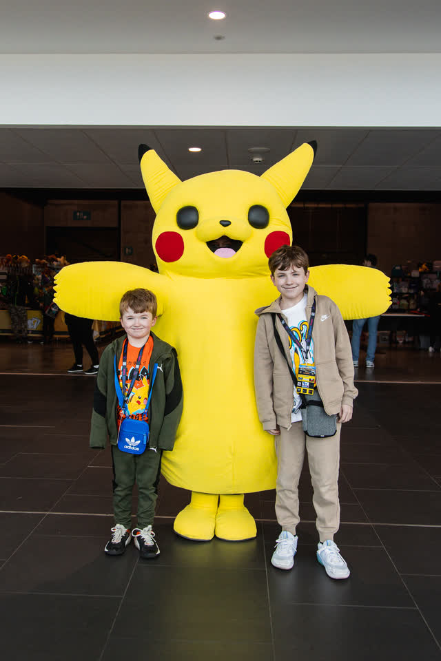Two children posing with a giant Pikachu mascot in the hall.