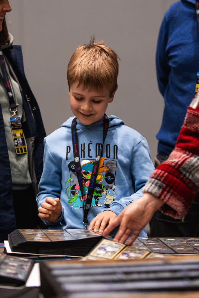 A boy in a Pokemon hoodie smiling down at a binder page on the table.