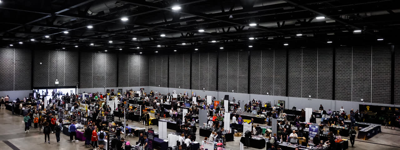 The whole hall seen from above, rows of trading tables spread across the floor under the lights.