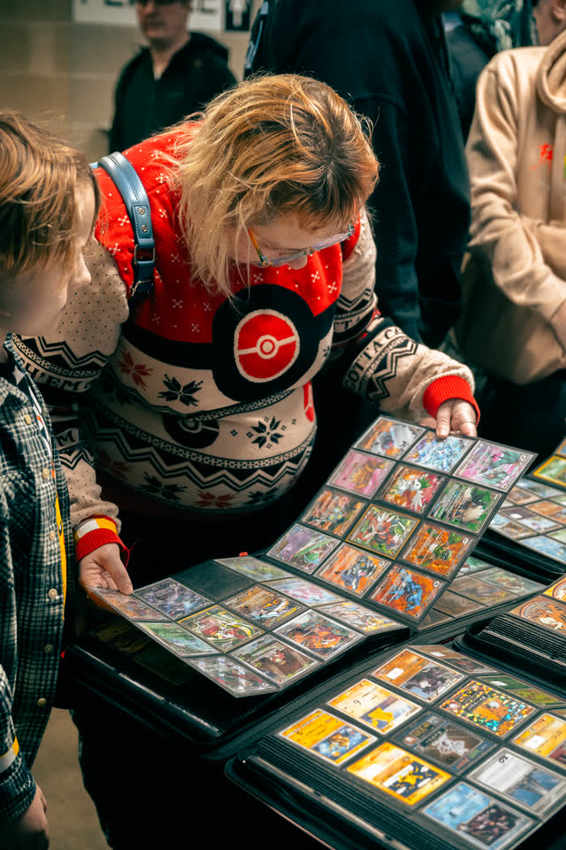 A collector in a Poke Ball Christmas jumper going through binder pages of holographic cards.