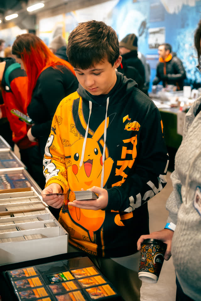 A boy in a Pikachu hoodie studying a card in his hand beside a box of singles.