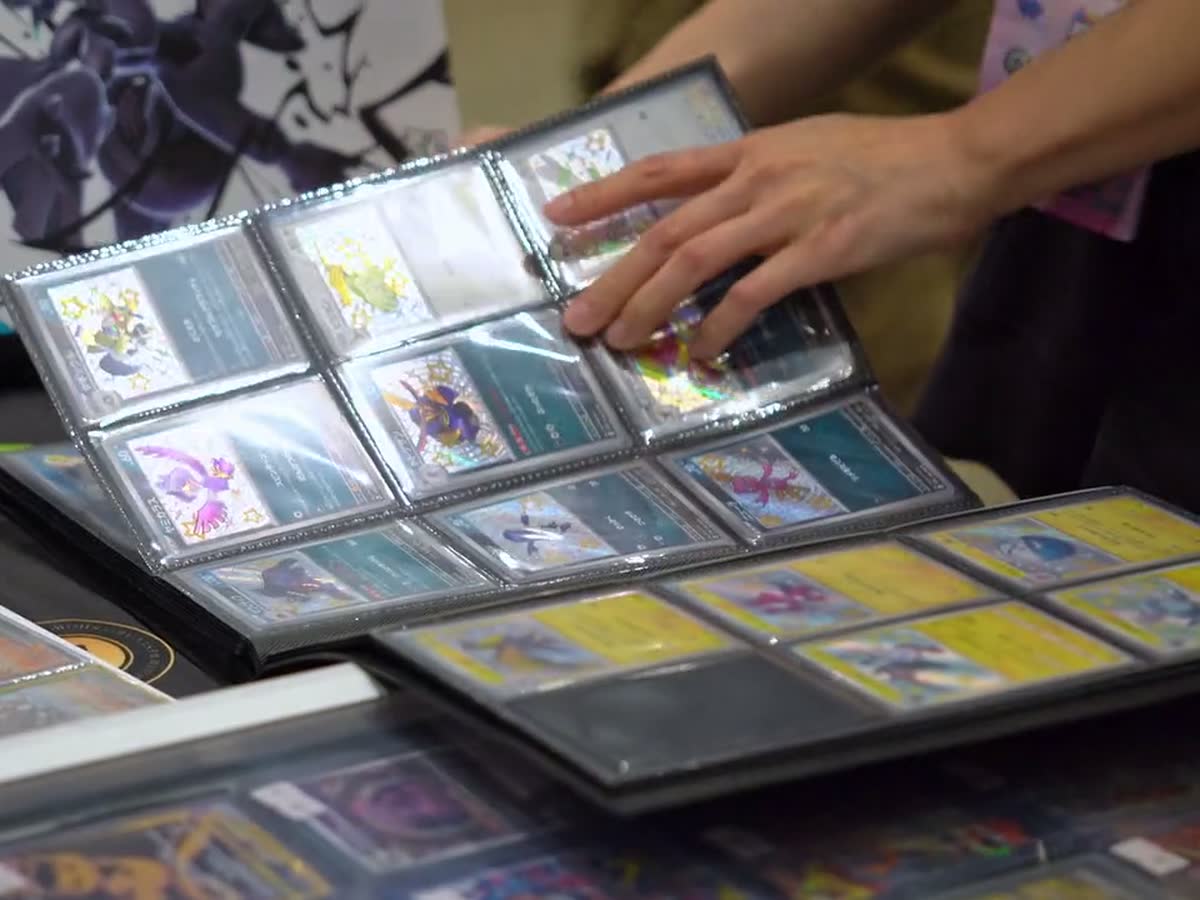 Hands turning binder pages of sleeved cards across a table, pointing out a pick.