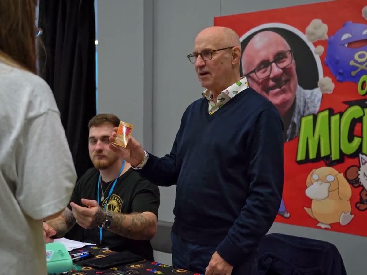 A guest talking with collectors at a signing table in front of his banner.